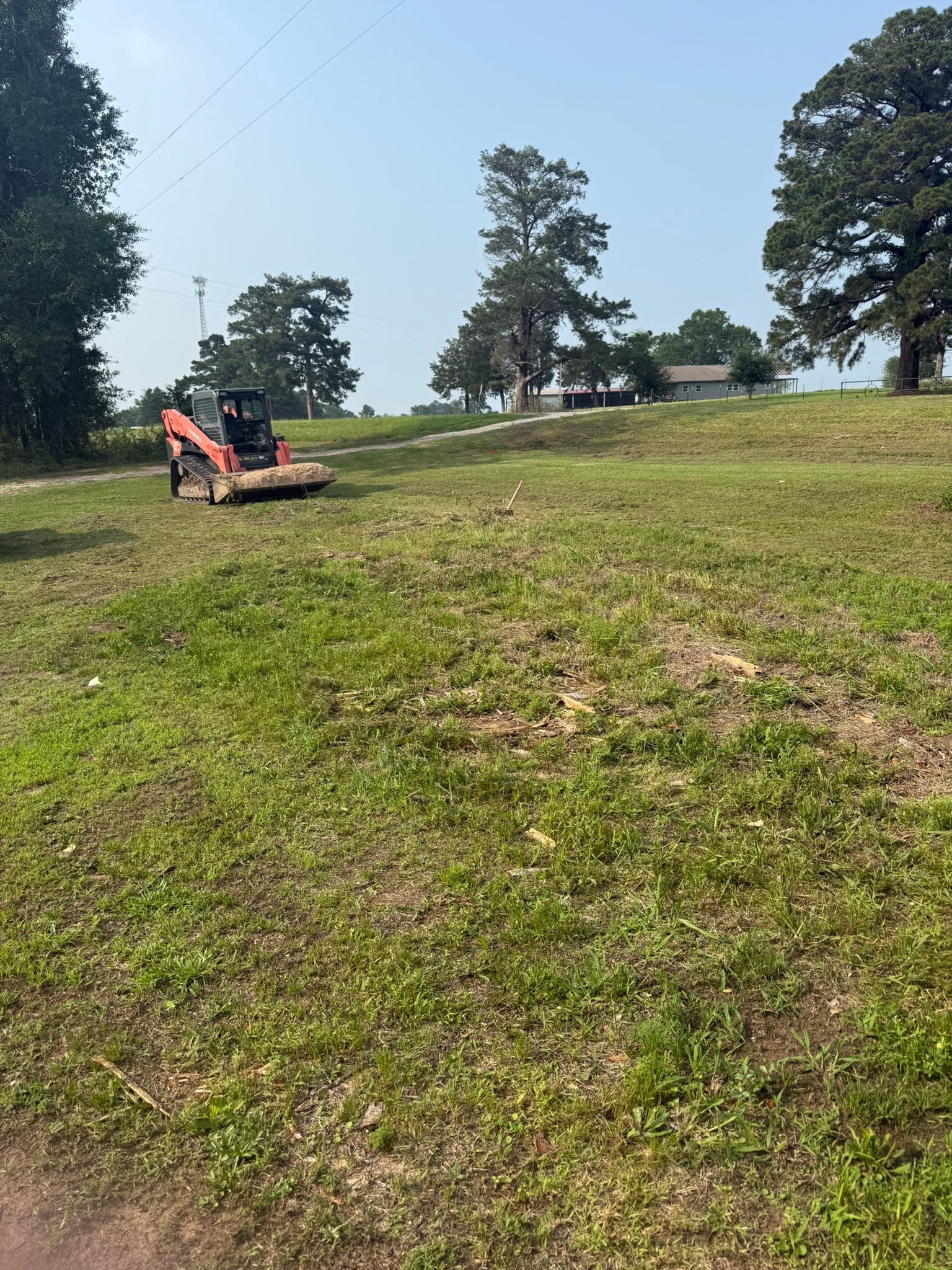 Person operating an orange mower on a grassy hillside under a blue sky.