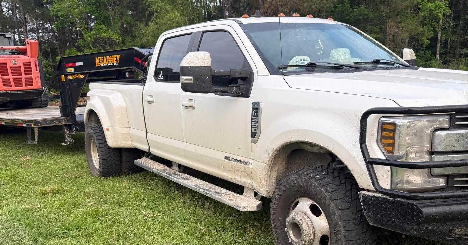 White heavy-duty pickup truck parked on grass beside a work trailer