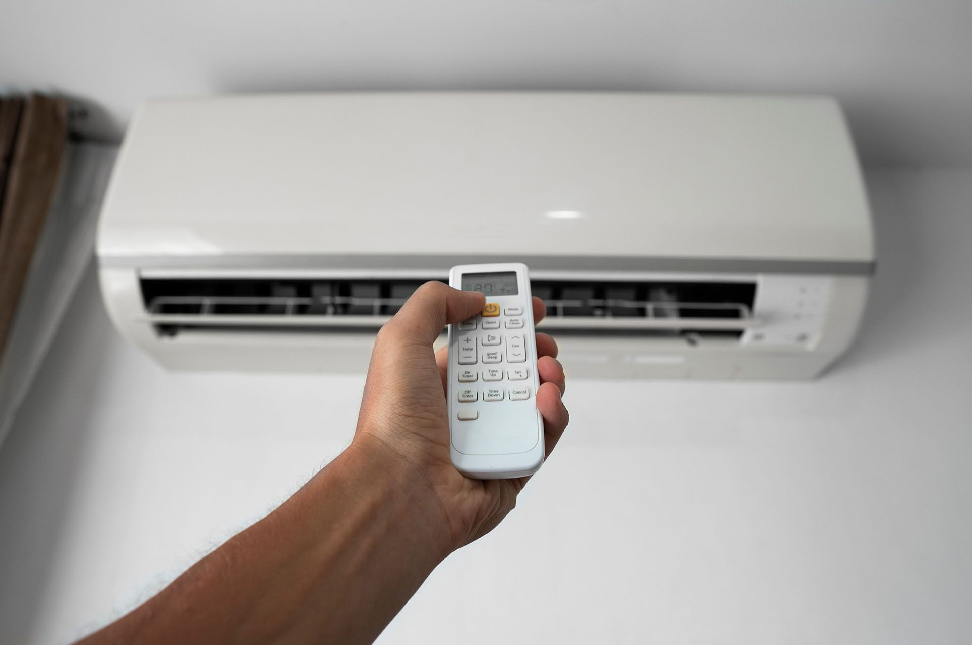 A person is holding a remote control in front of an air conditioner