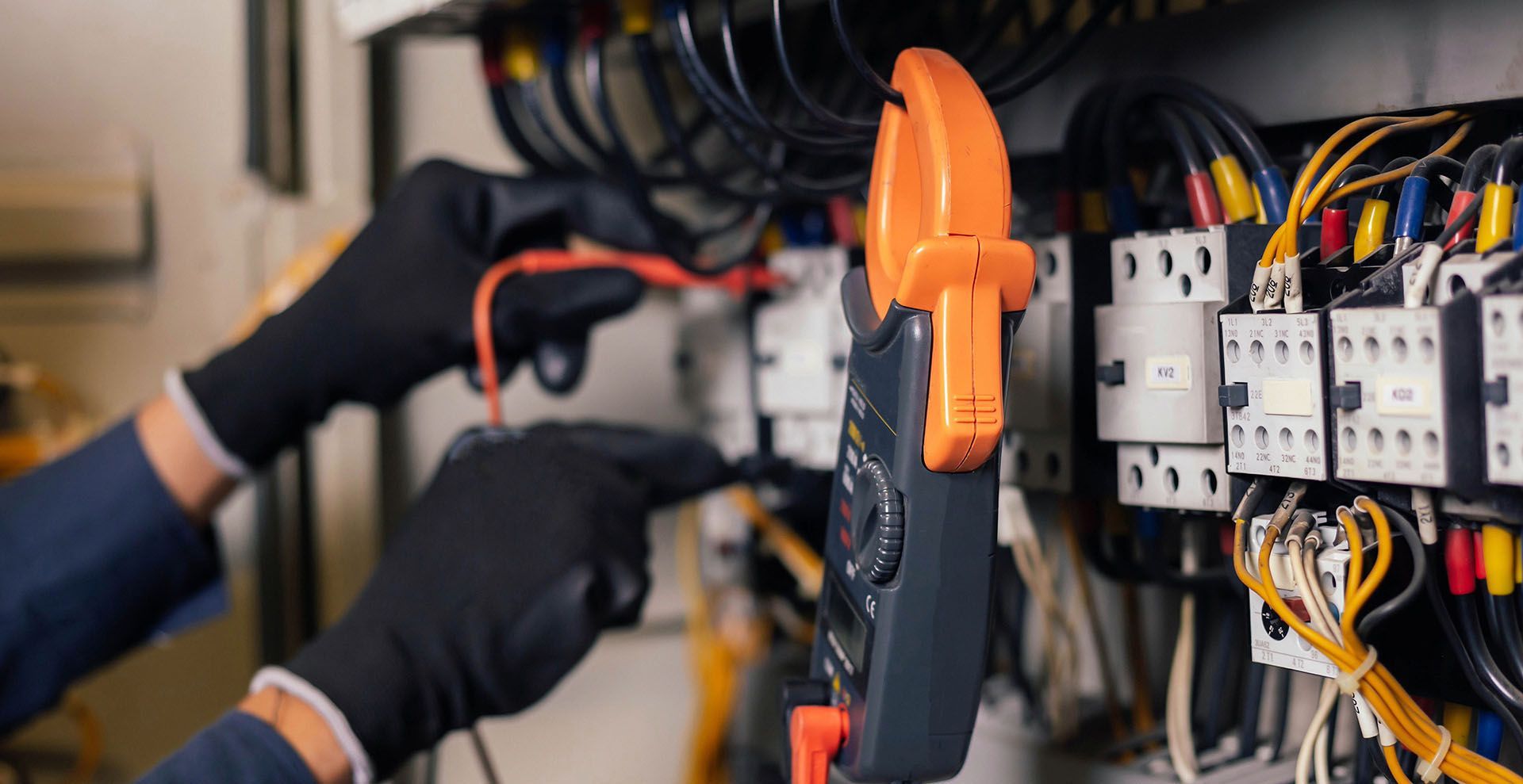 An electrician is working on an electrical panel with a clamp.
