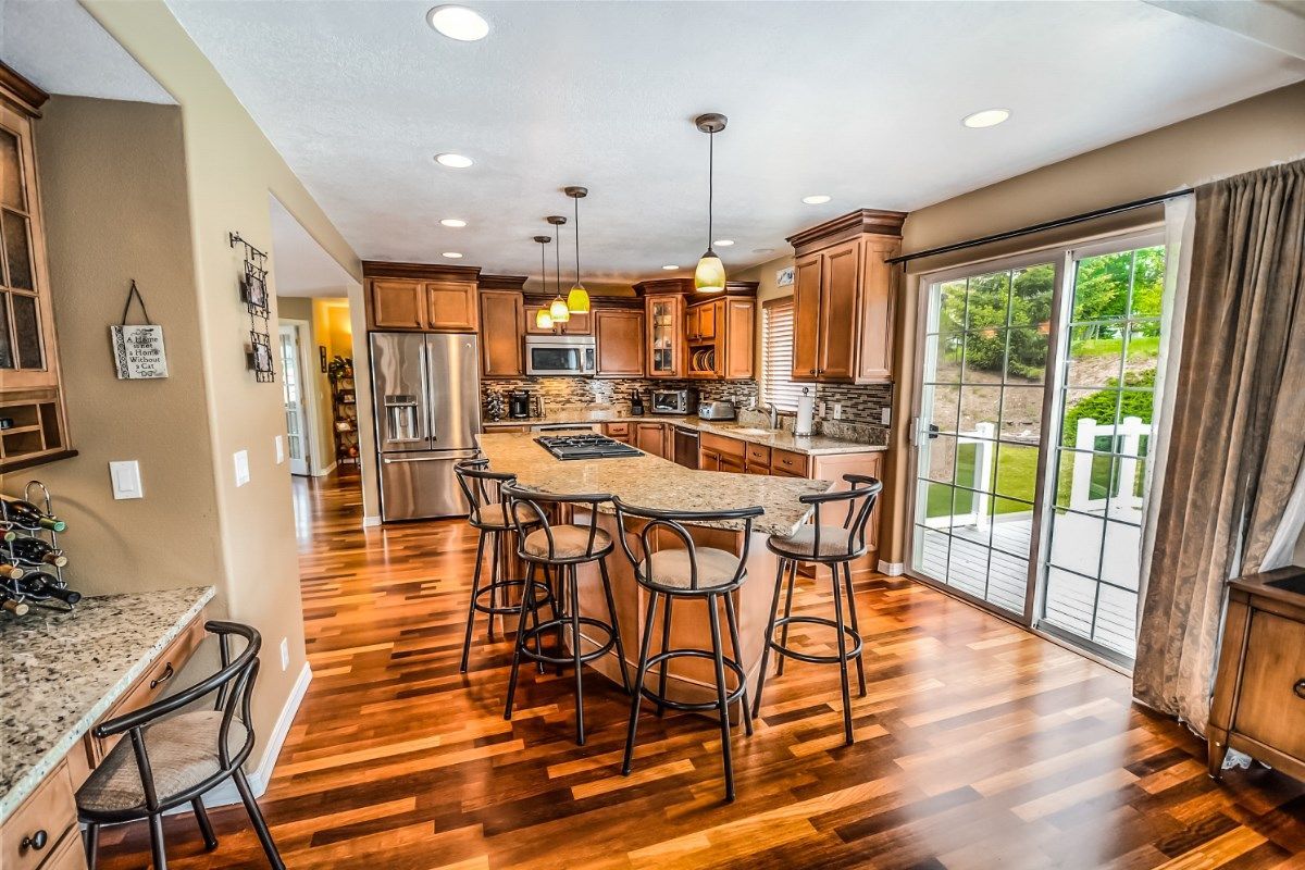 Kitchen with wooden floors, island with stools, cabinets, and sliding glass door to a backyard.