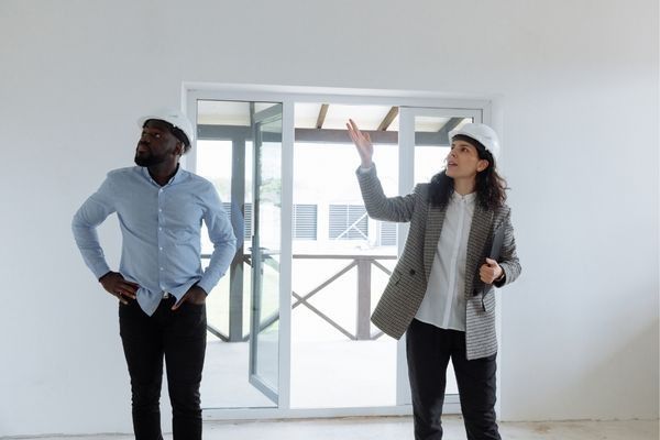 Two people in hard hats inspecting a room. One points up, the other looks up with his hands on his hips.