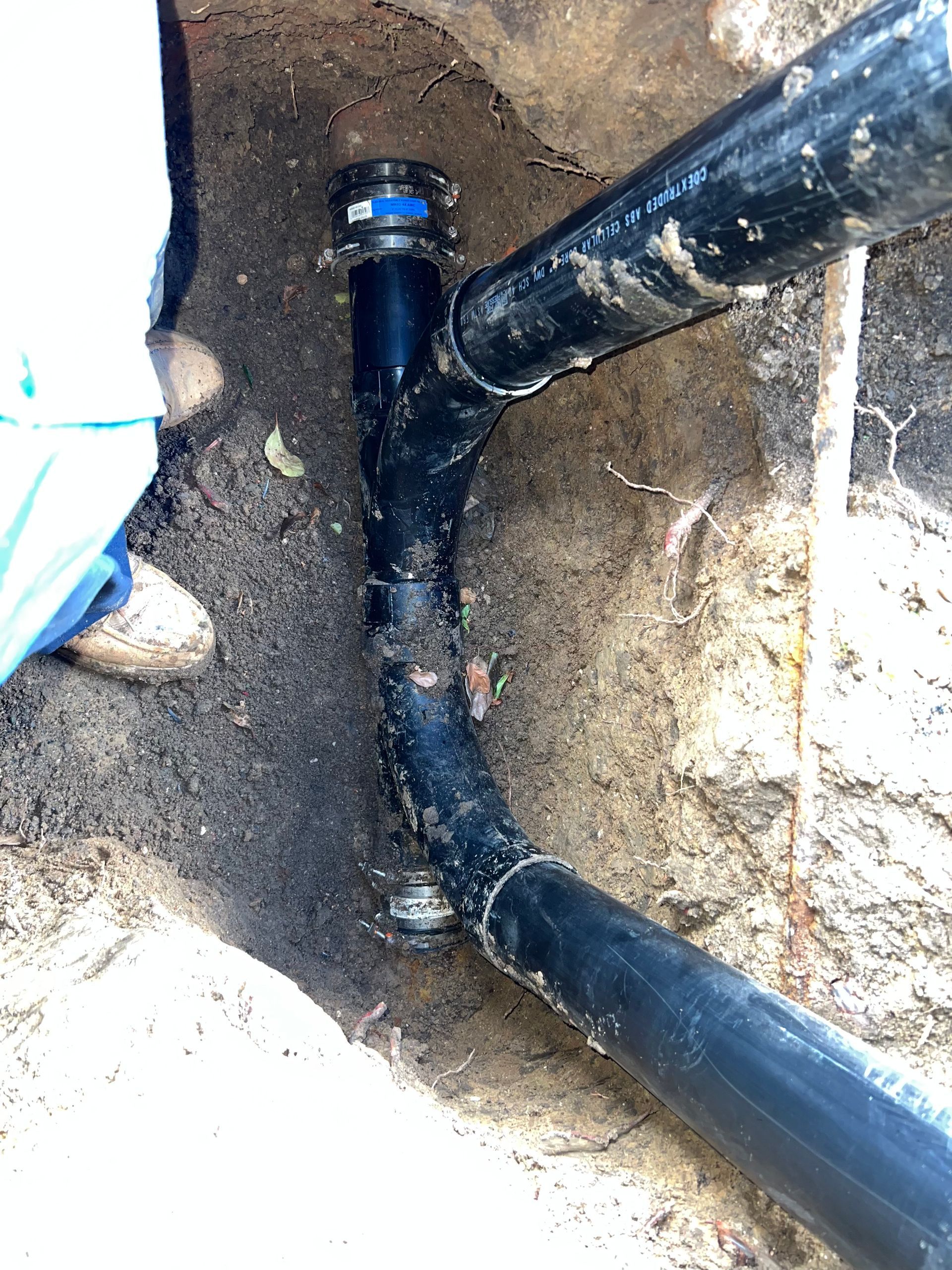Black plastic pipes joined in a dirt trench with a blue connector cap.
