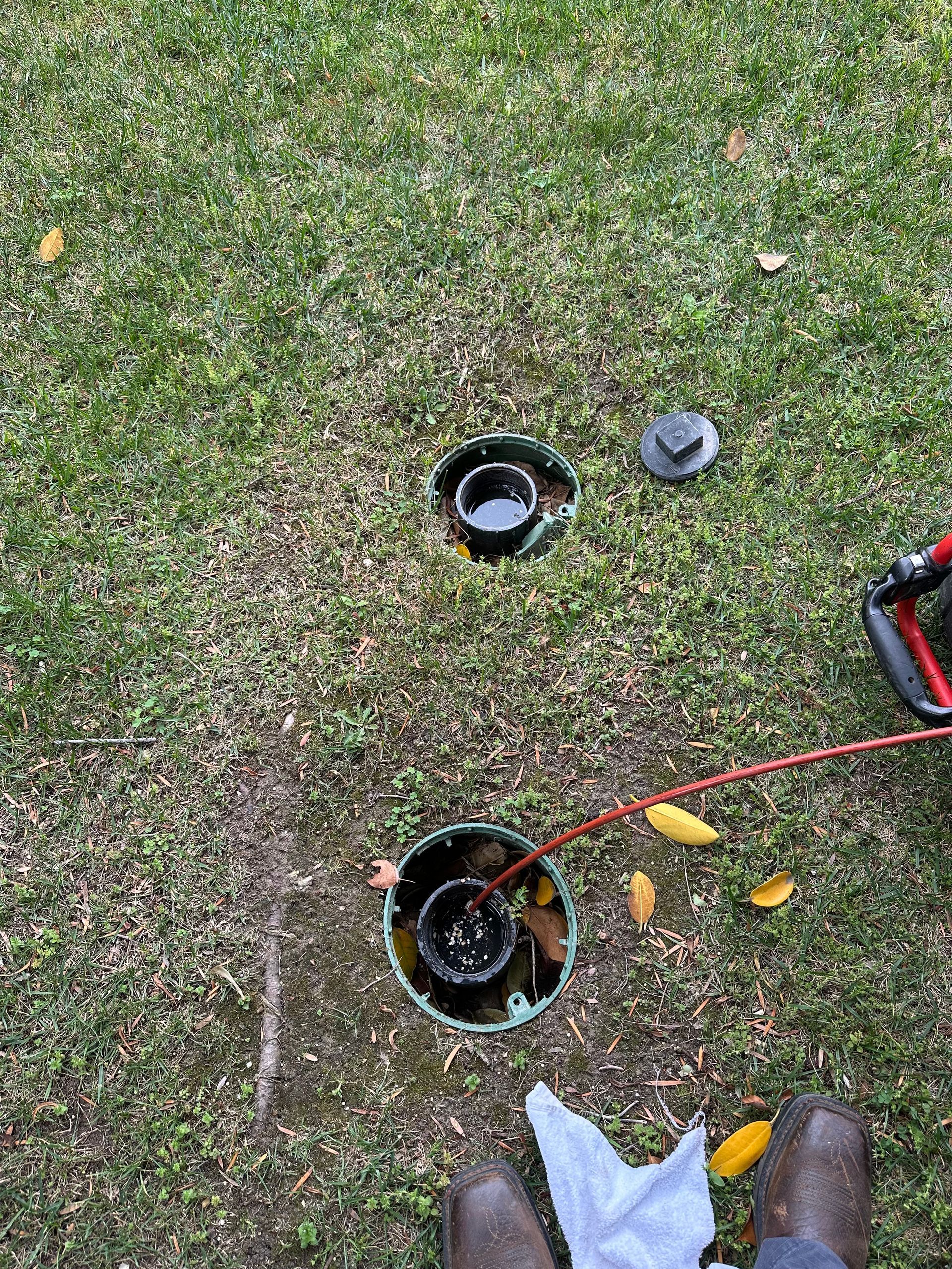 Two open utility holes in grass, one with a red cable and a white bag nearby.