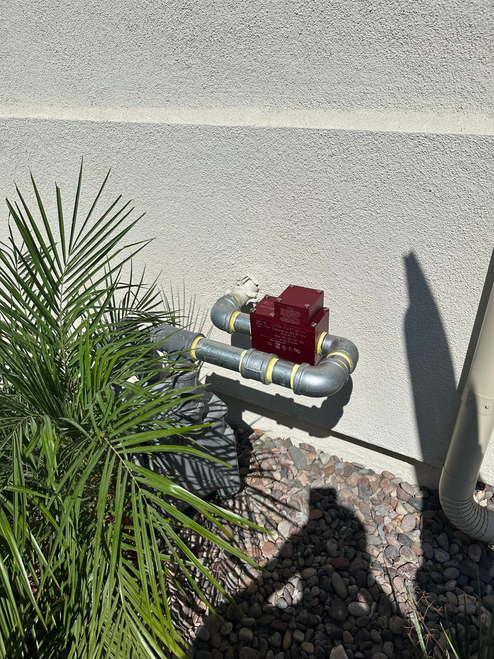 Gas meter and red valve on an exterior stucco wall beside landscaping