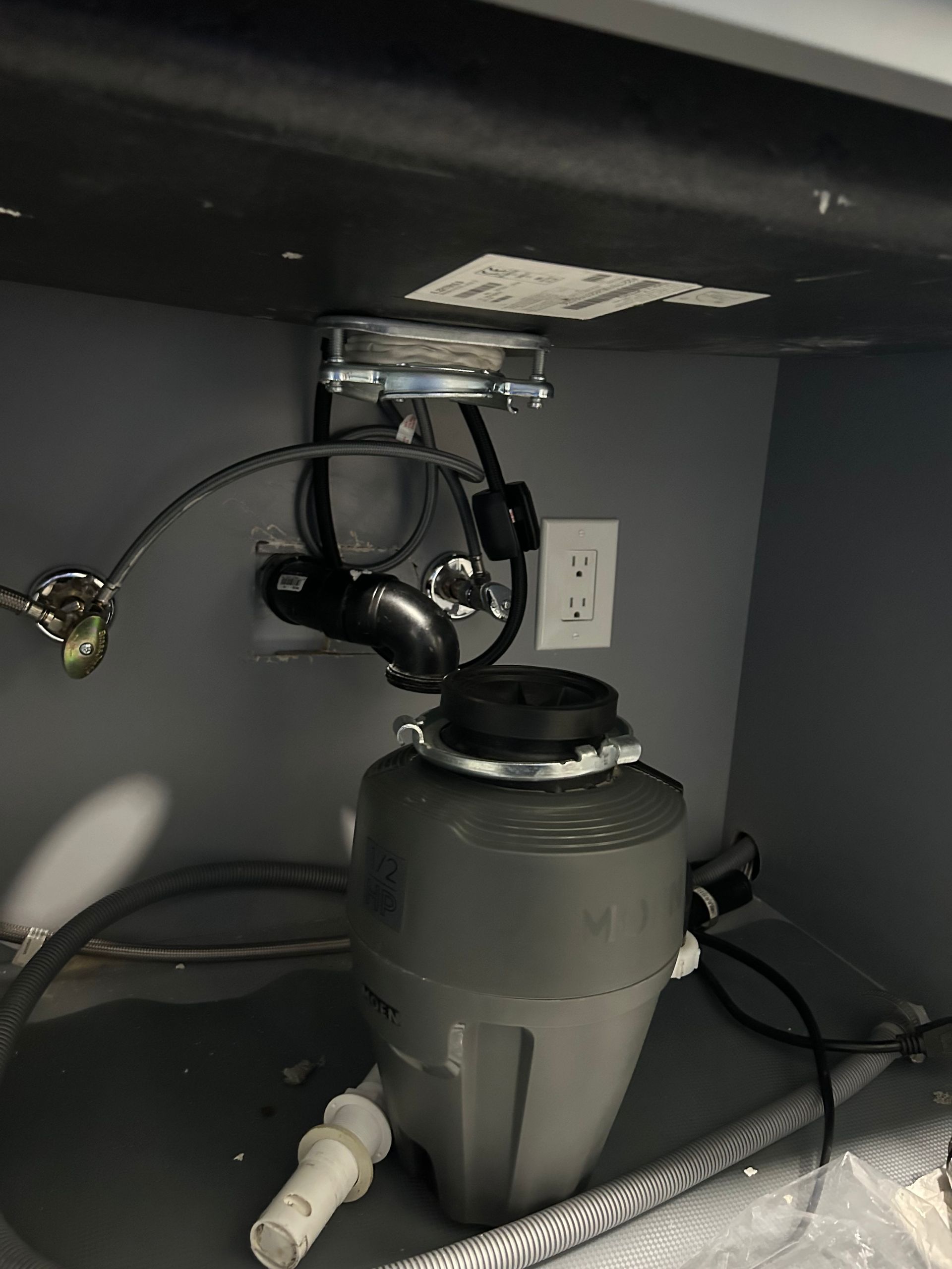 Under-sink garbage disposal with exposed plumbing, power cord, and outlet inside a cabinet