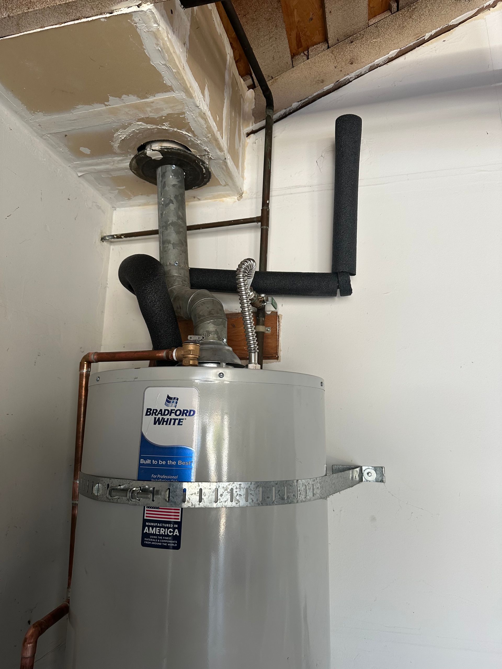Water heater with insulated pipes and a black exhaust vent in a utility closet.