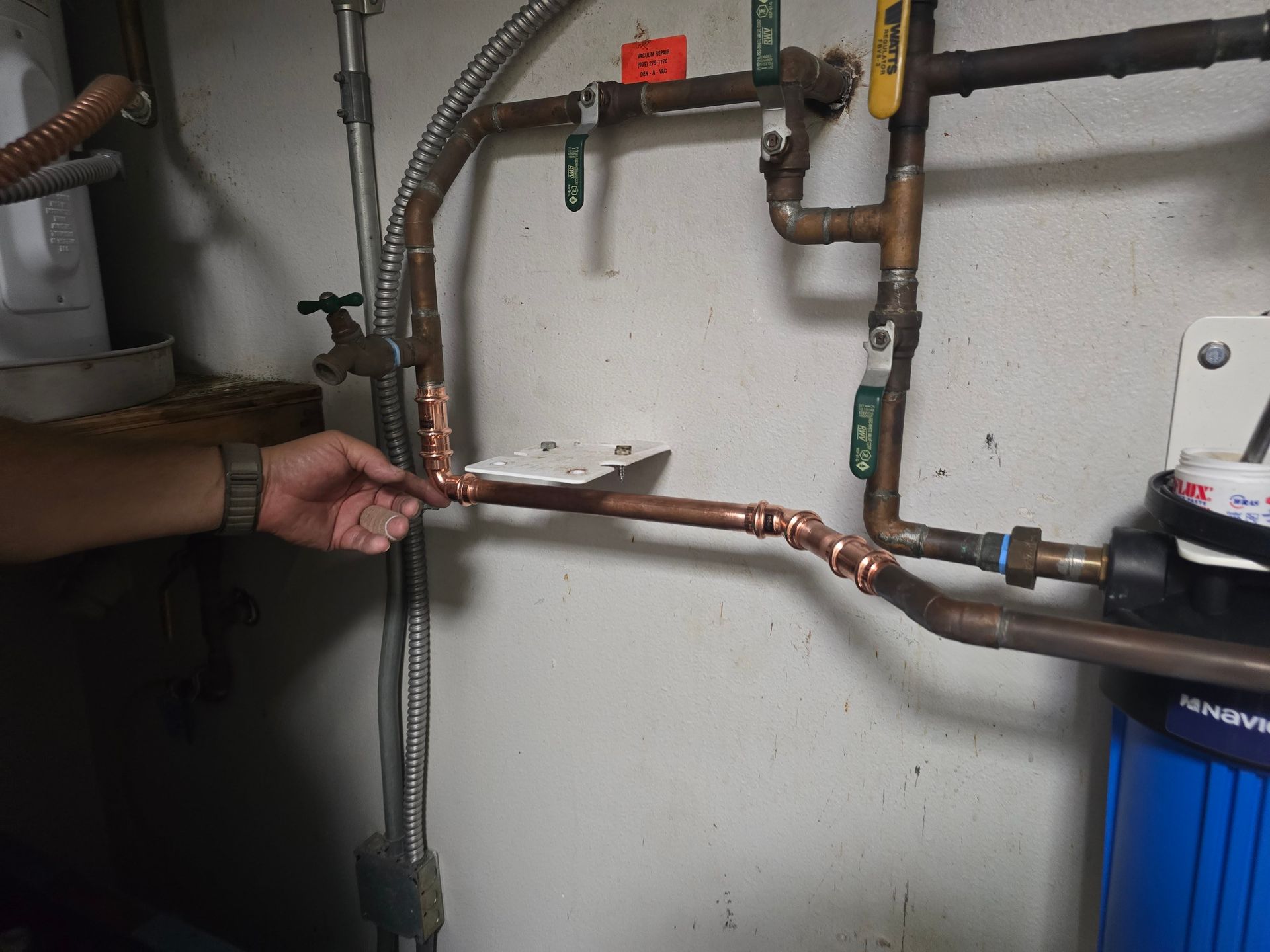 Hand holding a copper pipe in a basement utility area with exposed plumbing and a water heater