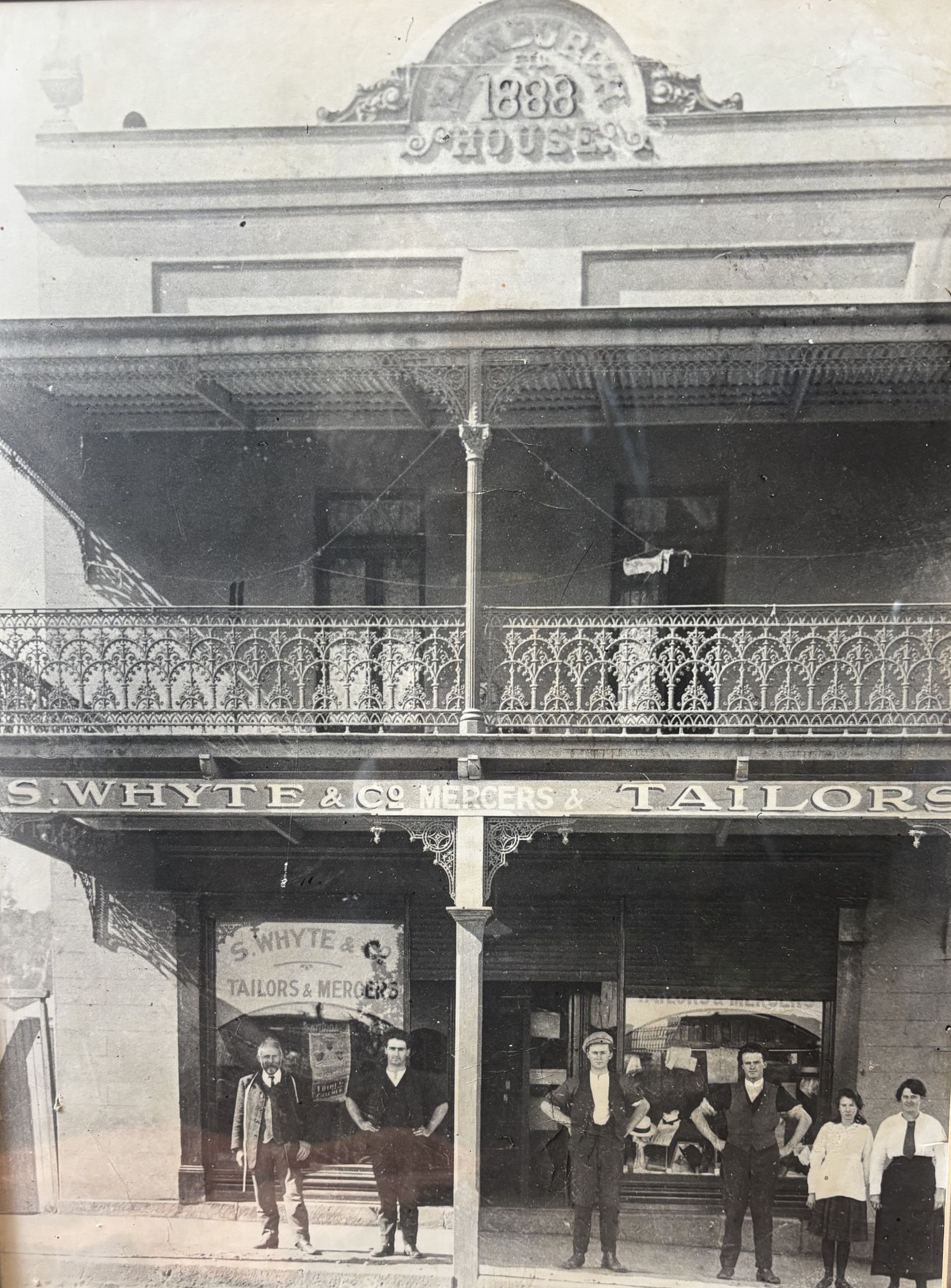 Historic storefront with ornate balcony and several people standing outside underneath