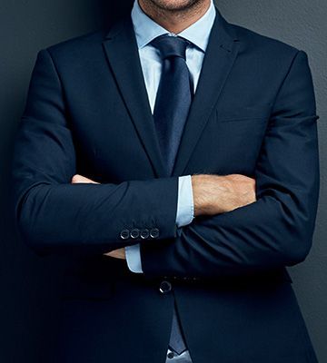Man in a navy suit with arms crossed against a dark blue background