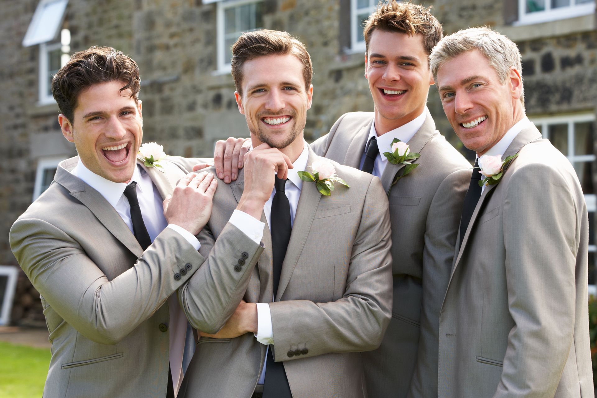 Four men in light suits smiling outdoors, holding hands and standing in front of houses.