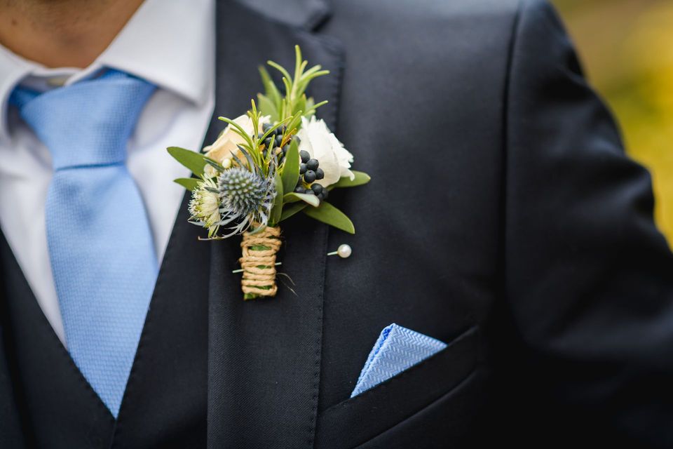 Close-up of a dark suit with a blue tie and pocket square, featuring a white floral boutonniere.