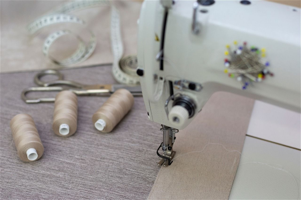 Sewing machine stitching fabric beside beige thread spools on a worktable