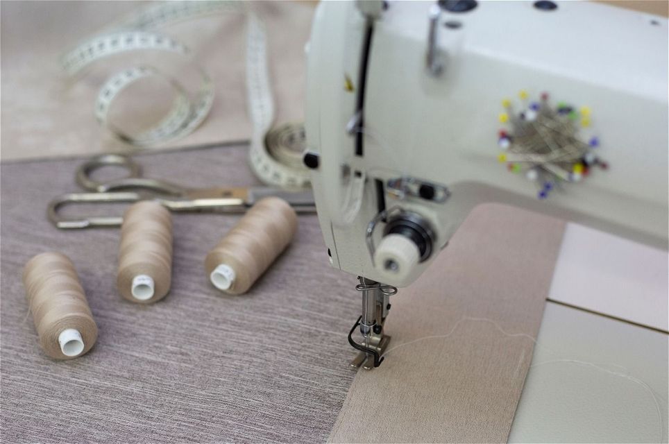 Close-up of a sewing machine stitching light fabric beside a spool of beige thread.