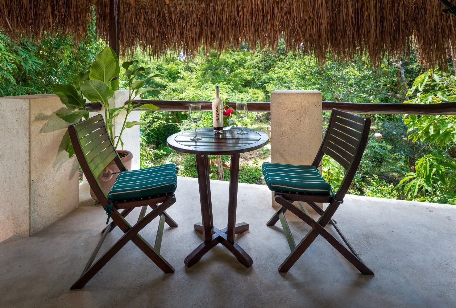 Thatched patio with two wooden chairs and a small round table overlooking lush greenery