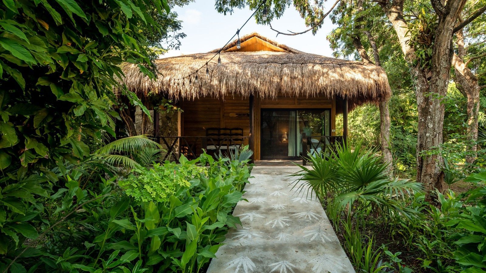 Tropical bungalow with a thatched roof, wooden deck, and lush green garden path