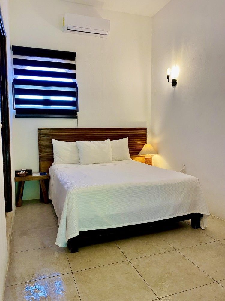 Simple bedroom with a neatly made bed, striped window blind, and wall sconce lighting