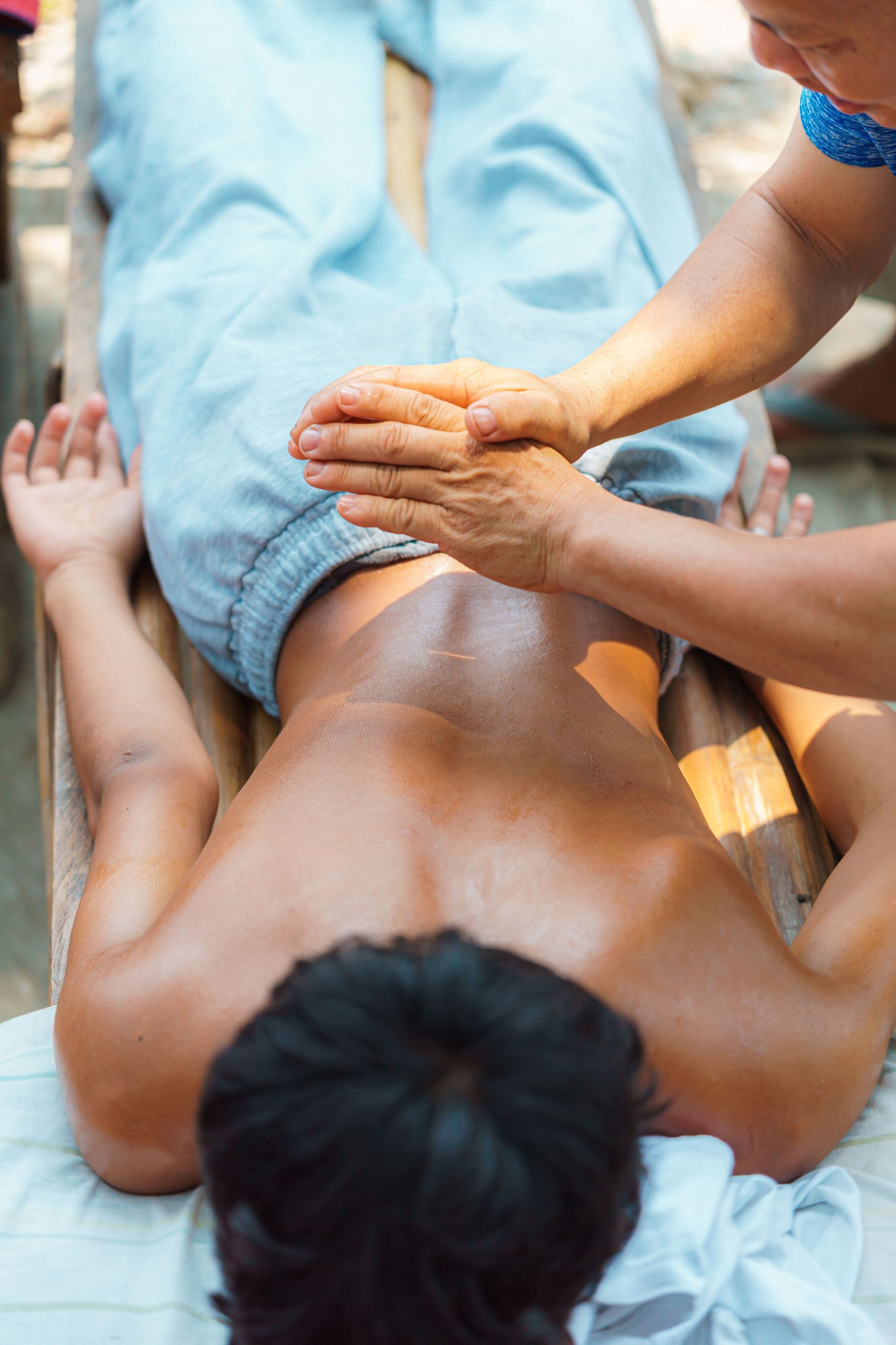 Person receiving a back massage on a mat, with hands pressing along the spine and legs visible in blue pants