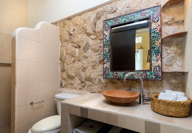 Small rustic bathroom with stone wall, decorative mirror, and sink counter with bowls and basket