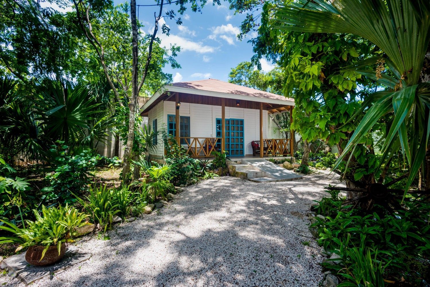 Small tropical bungalow with a gravel path, surrounded by lush green palms and trees.