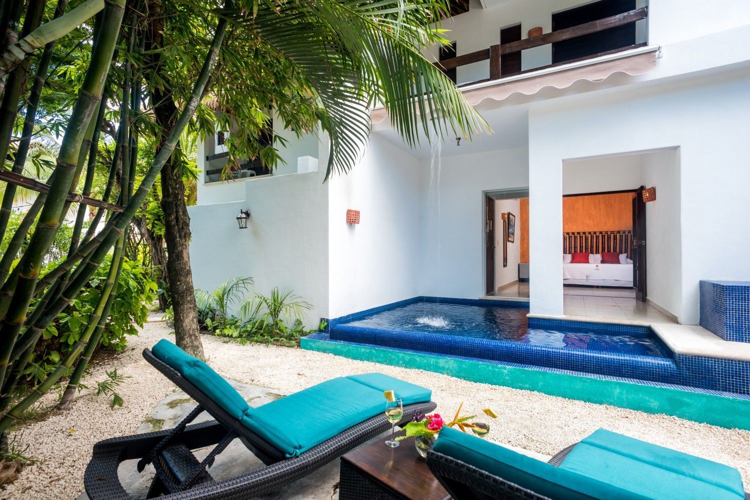 Tropical villa patio with turquoise lounge chairs and a small pool beside a white house