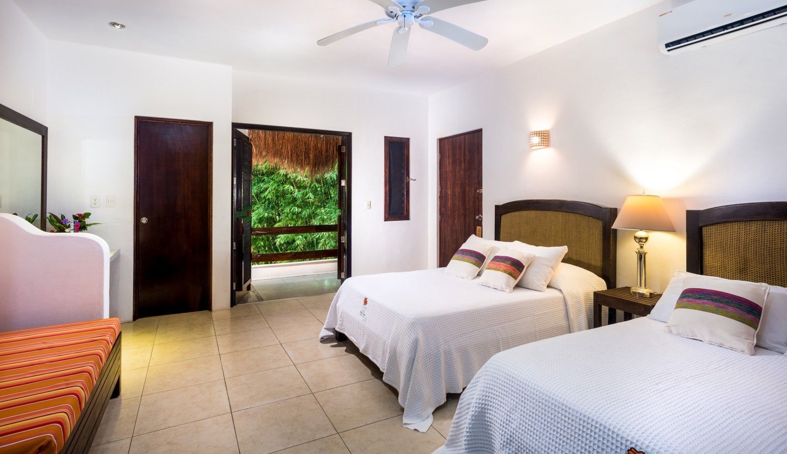 Bright bedroom with two twin beds, white walls, and an open doorway to greenery outdoors