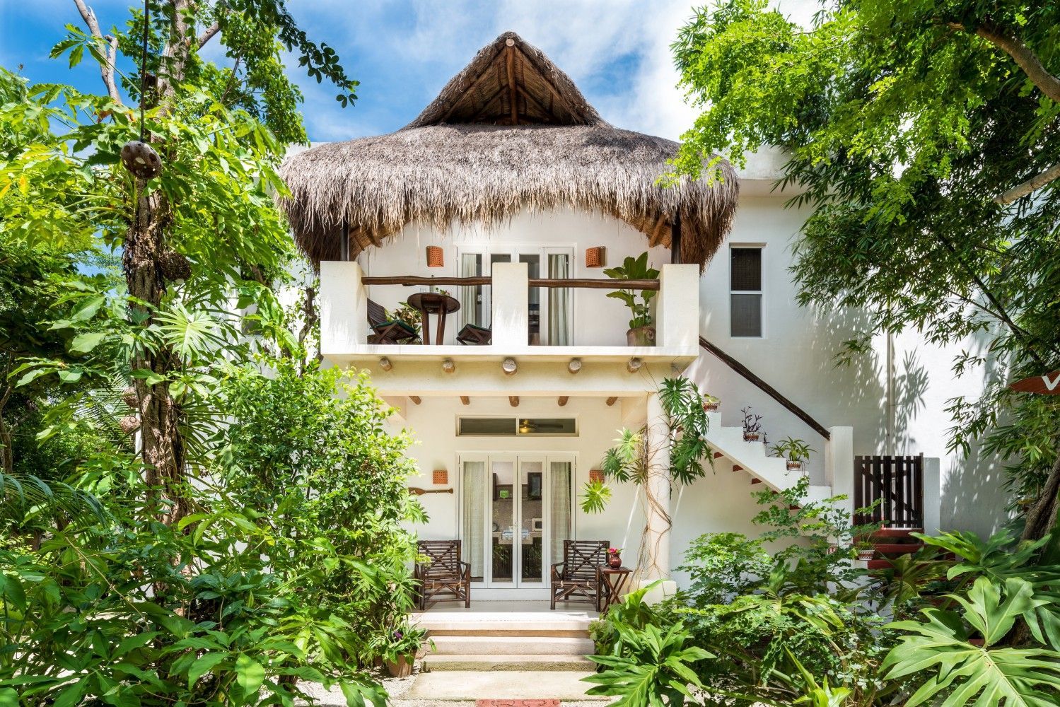 Tropical white house with thatched roof surrounded by lush green trees and plants