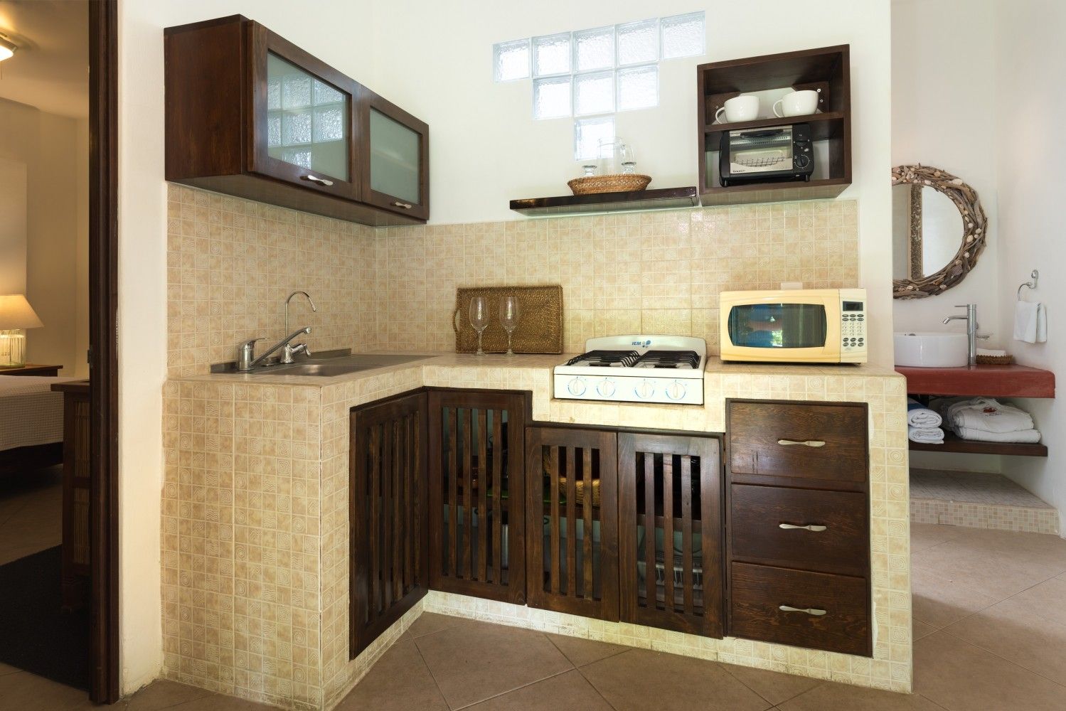 Compact kitchen nook with beige counters, dark wood cabinets, and a microwave by a window.