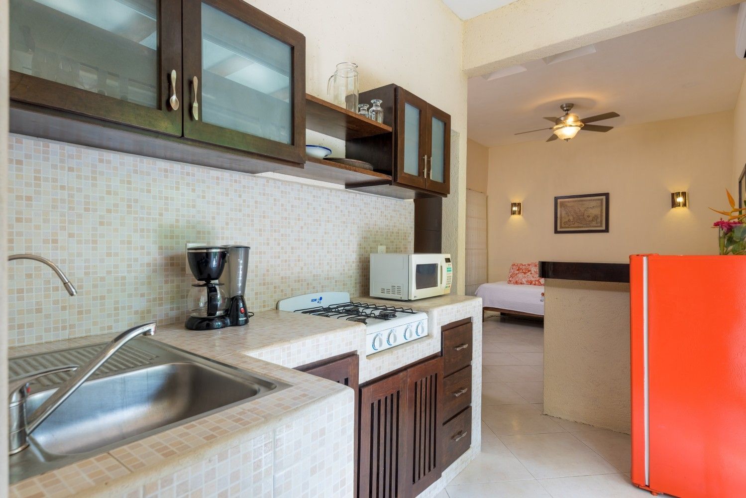 Small kitchen with sink, microwave, coffee maker, and red refrigerator opening into a cozy living area