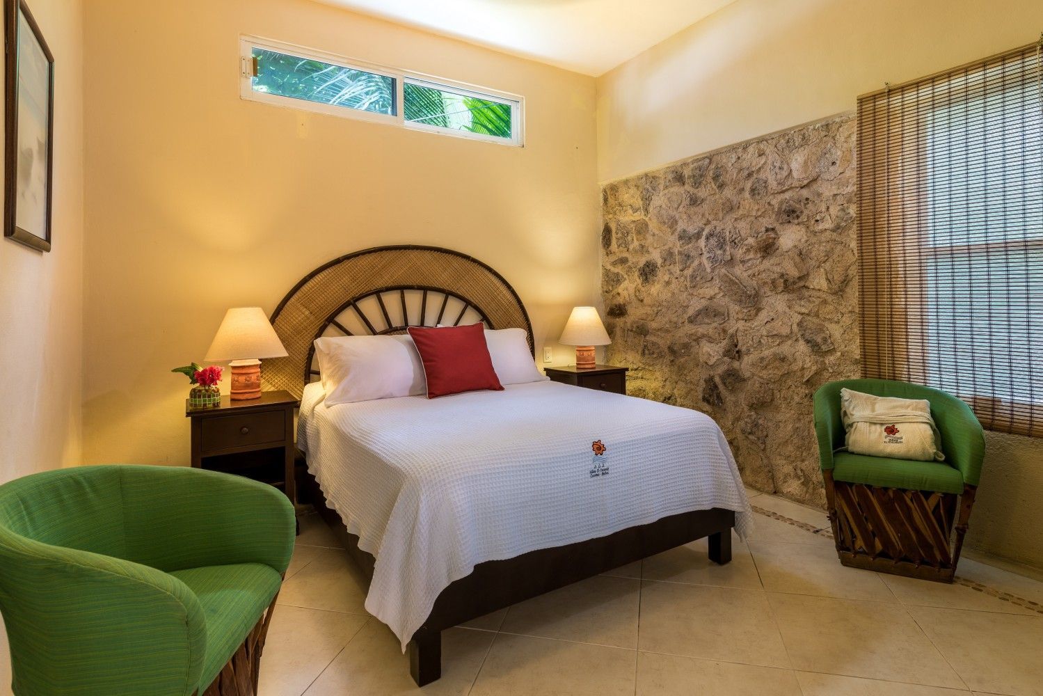 Cozy bedroom with a bed, green chairs, bedside lamps, and warm beige walls.