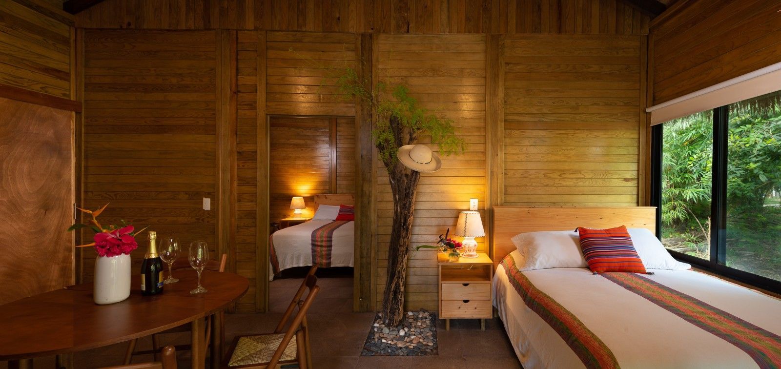 Cozy bamboo bedroom with two beds, warm lamps, and a view of greenery outside the window
