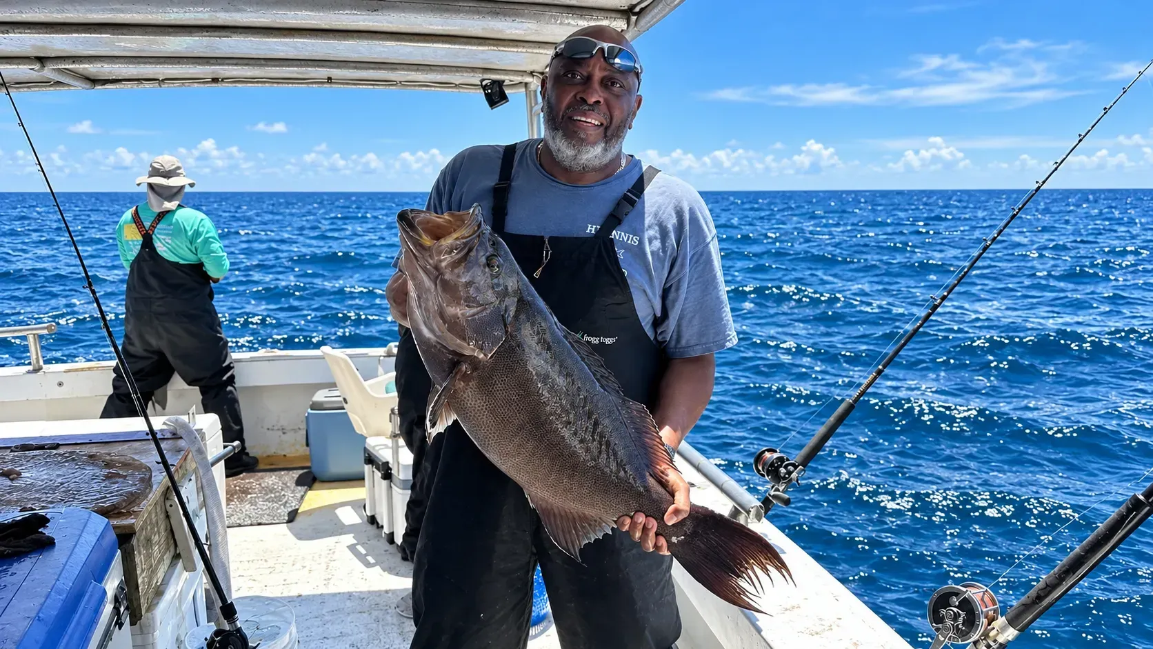 Man holding a large fish on a fishing boat with ocean and blue sky in the background
