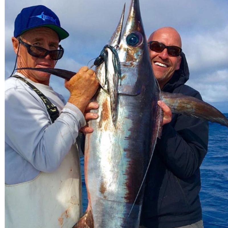 Two anglers smiling while holding a large tuna on a boat at sea