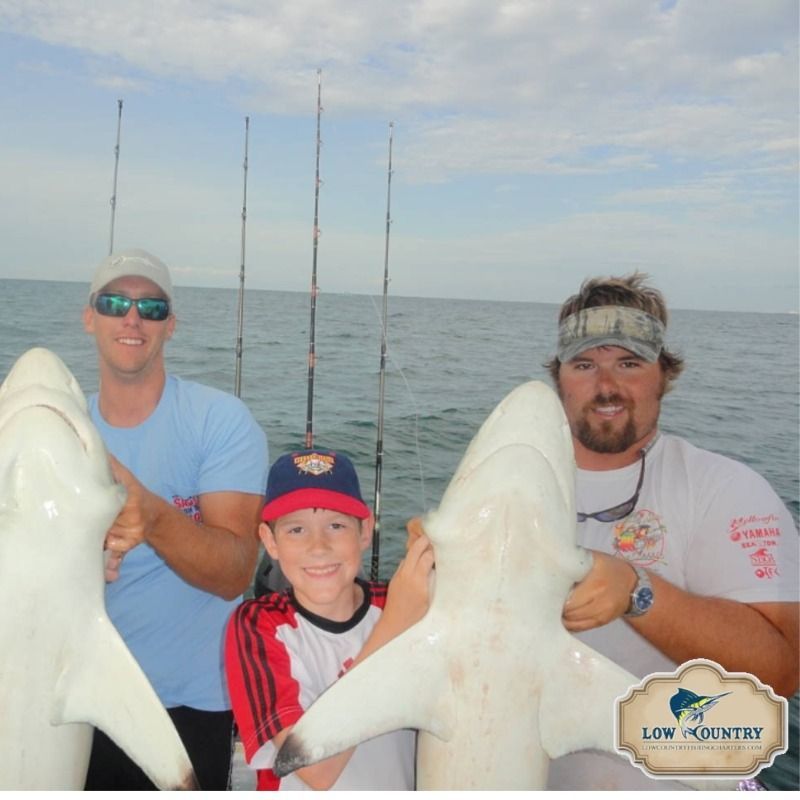 Three people hold large fish on a boat at sea, with fishing rods and open water behind them.