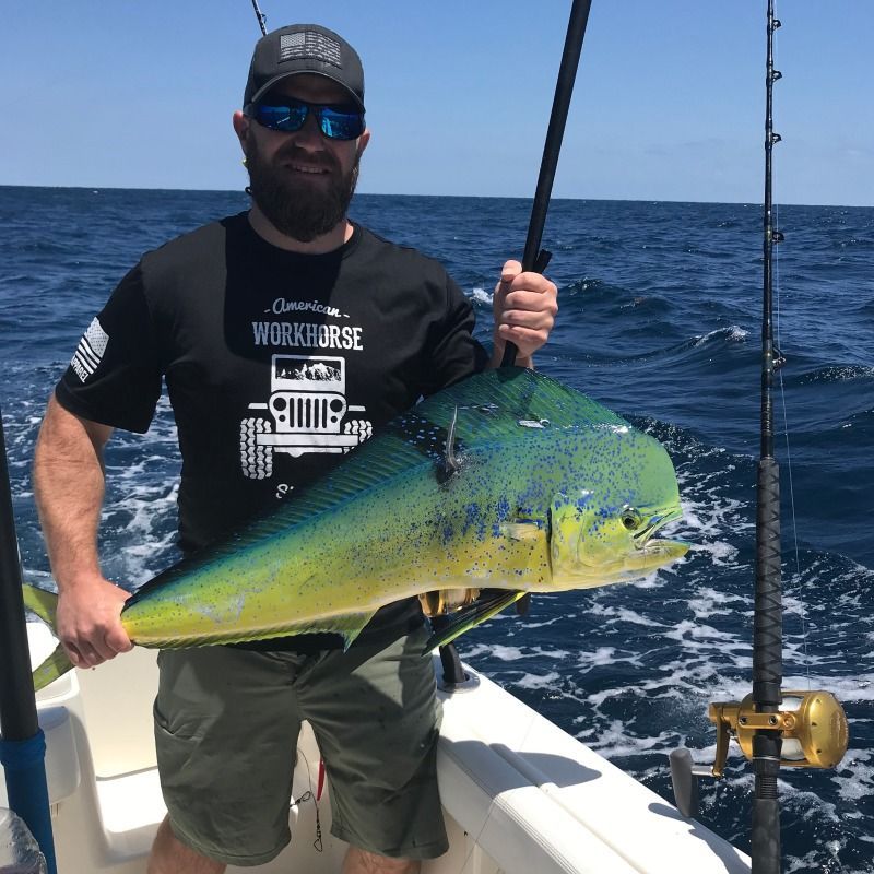 Angler holding a large green-yellow mahi-mahi on a fishing boat at sea