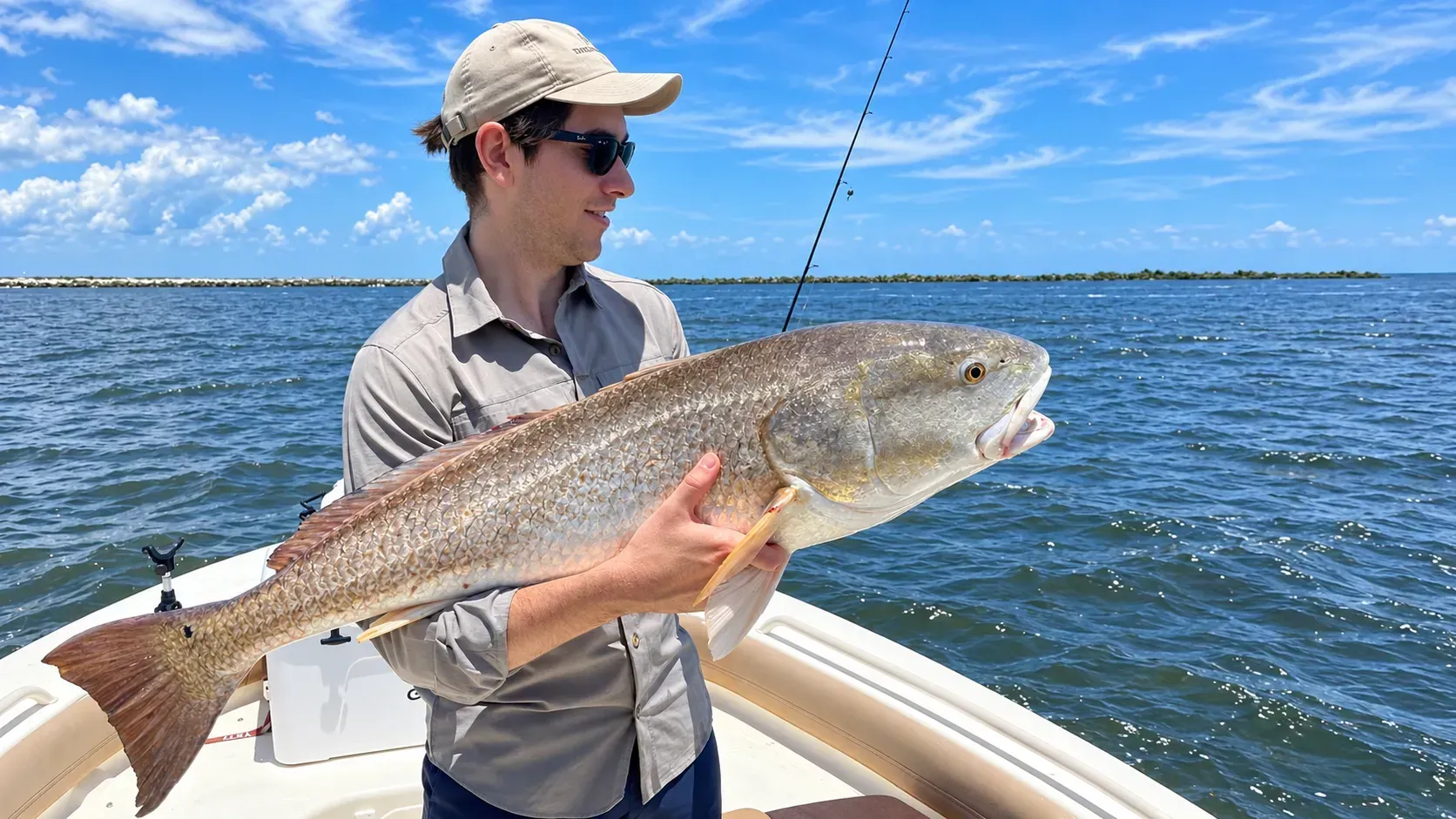 Angler holding a large fish on a boat in open water under a clear blue sky