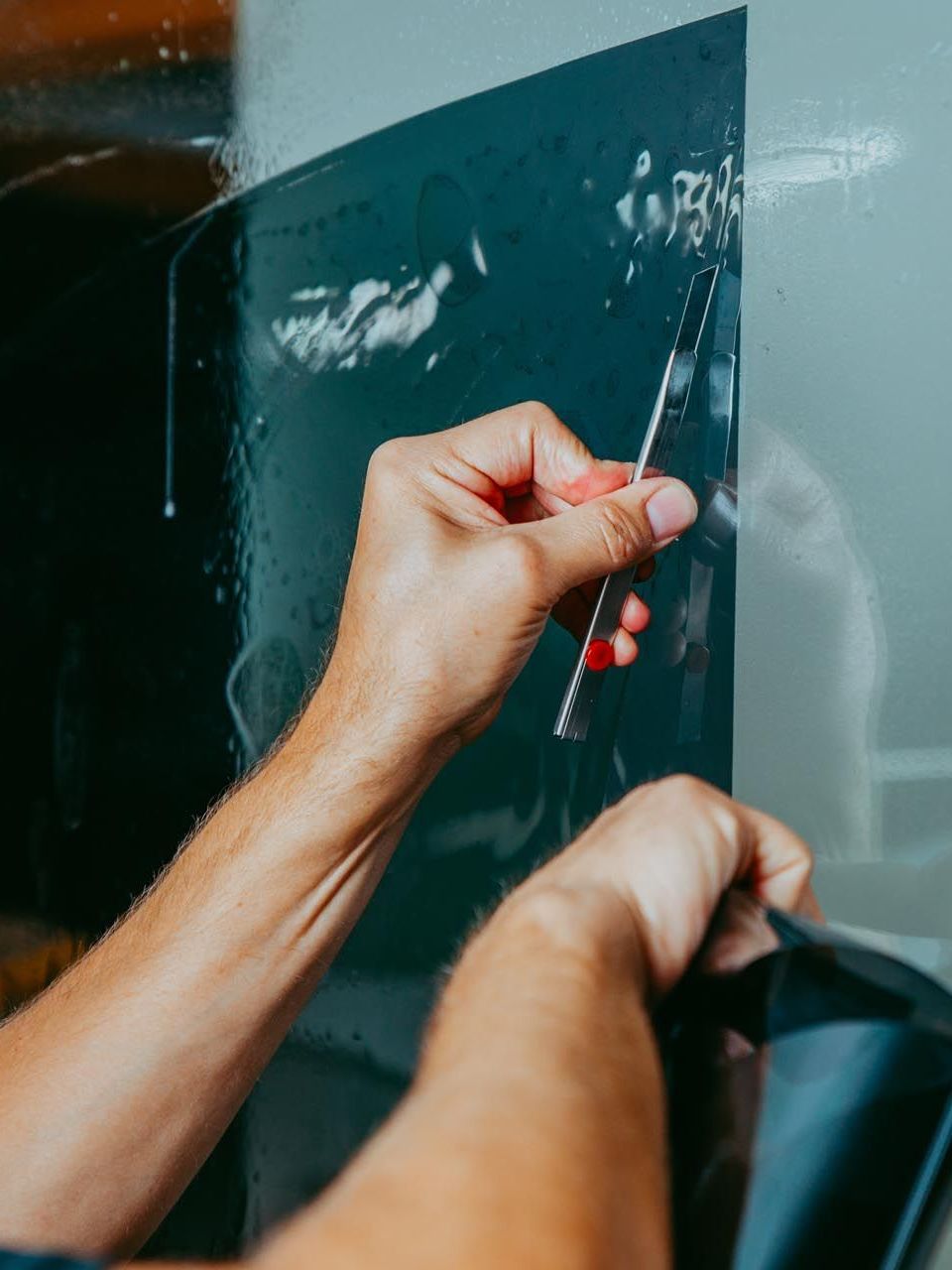 A person is applying a tinted window film to a car window.