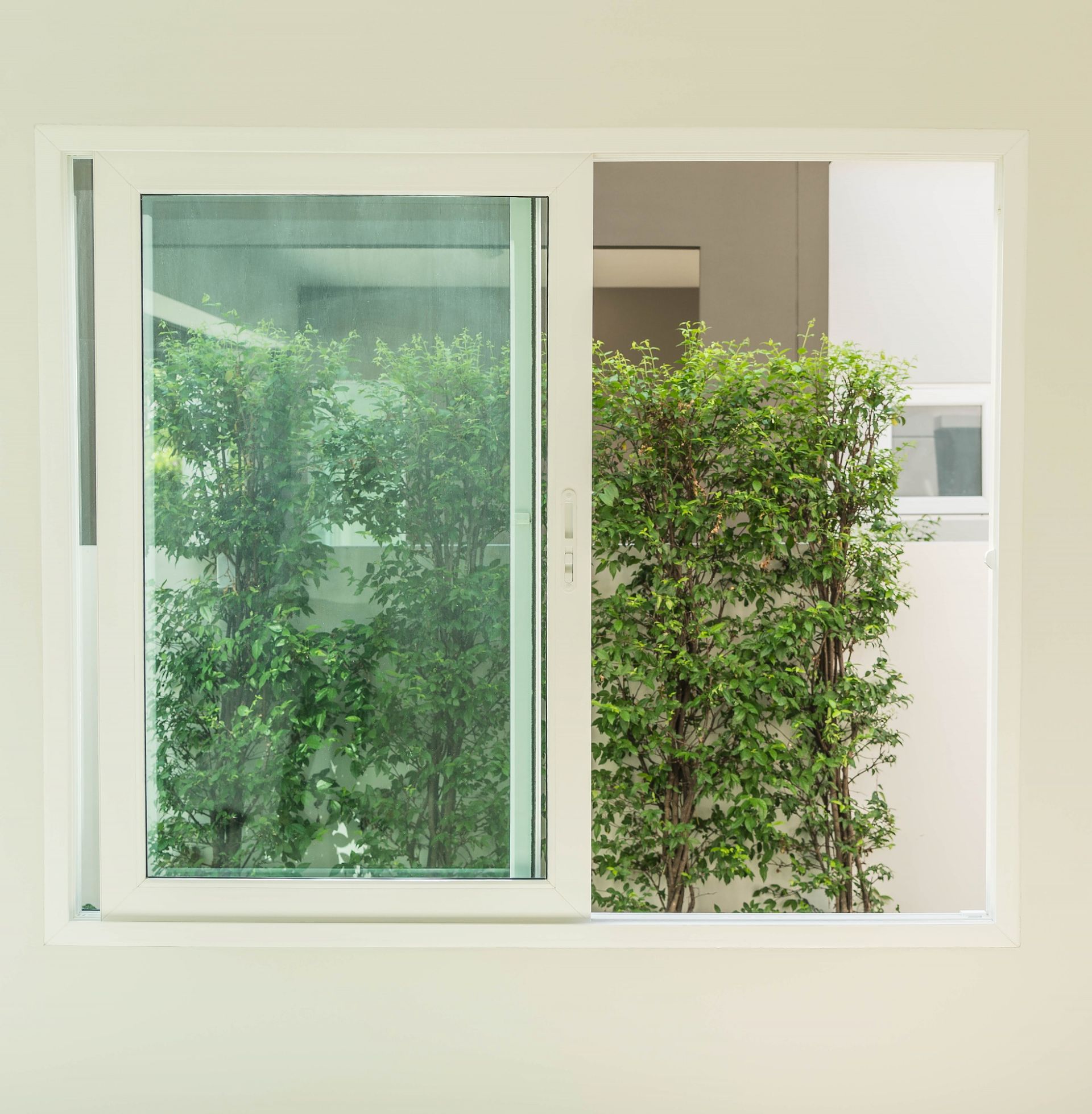 A white sliding glass window with a hedge in the background.