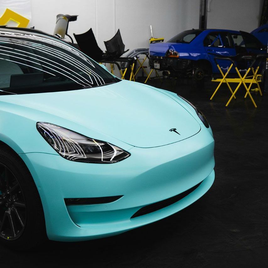 A light blue tesla model 3 is parked in a garage