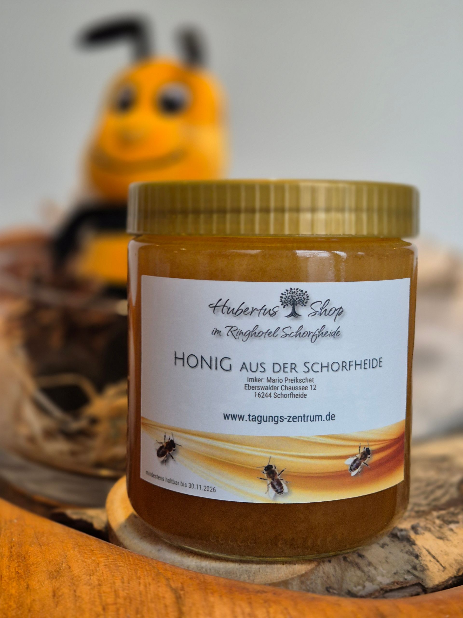 Honigglas mit Aufschrift „Honig aus der Schöberl“ vor unscharfer Bienendekoration.