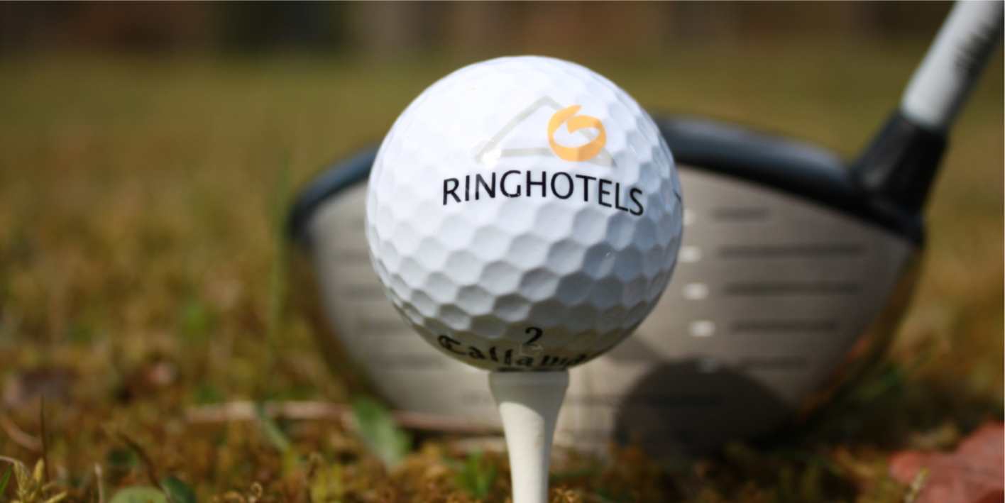 Golfball auf einem Tee, mit einem Driver im Hintergrund, auf einer Wiese.