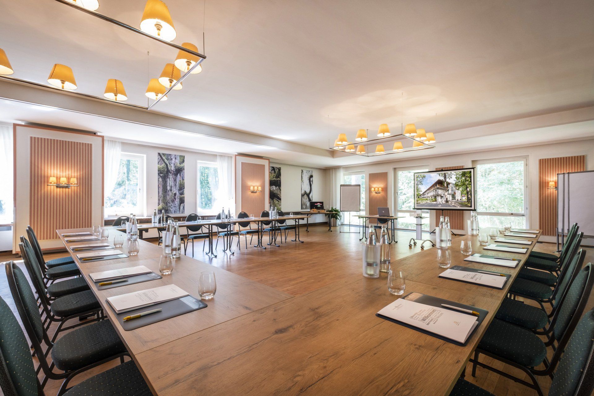 Konferenzraum mit langem Holztisch, Stühlen und einer Projektionsleinwand.