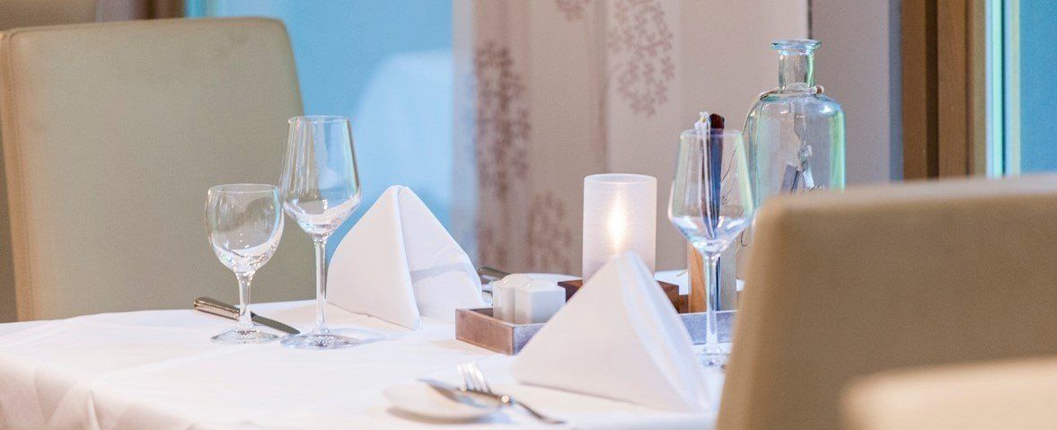 Tischdekoration in einem Restaurant mit Weingläsern, Servietten und einer Kerze.