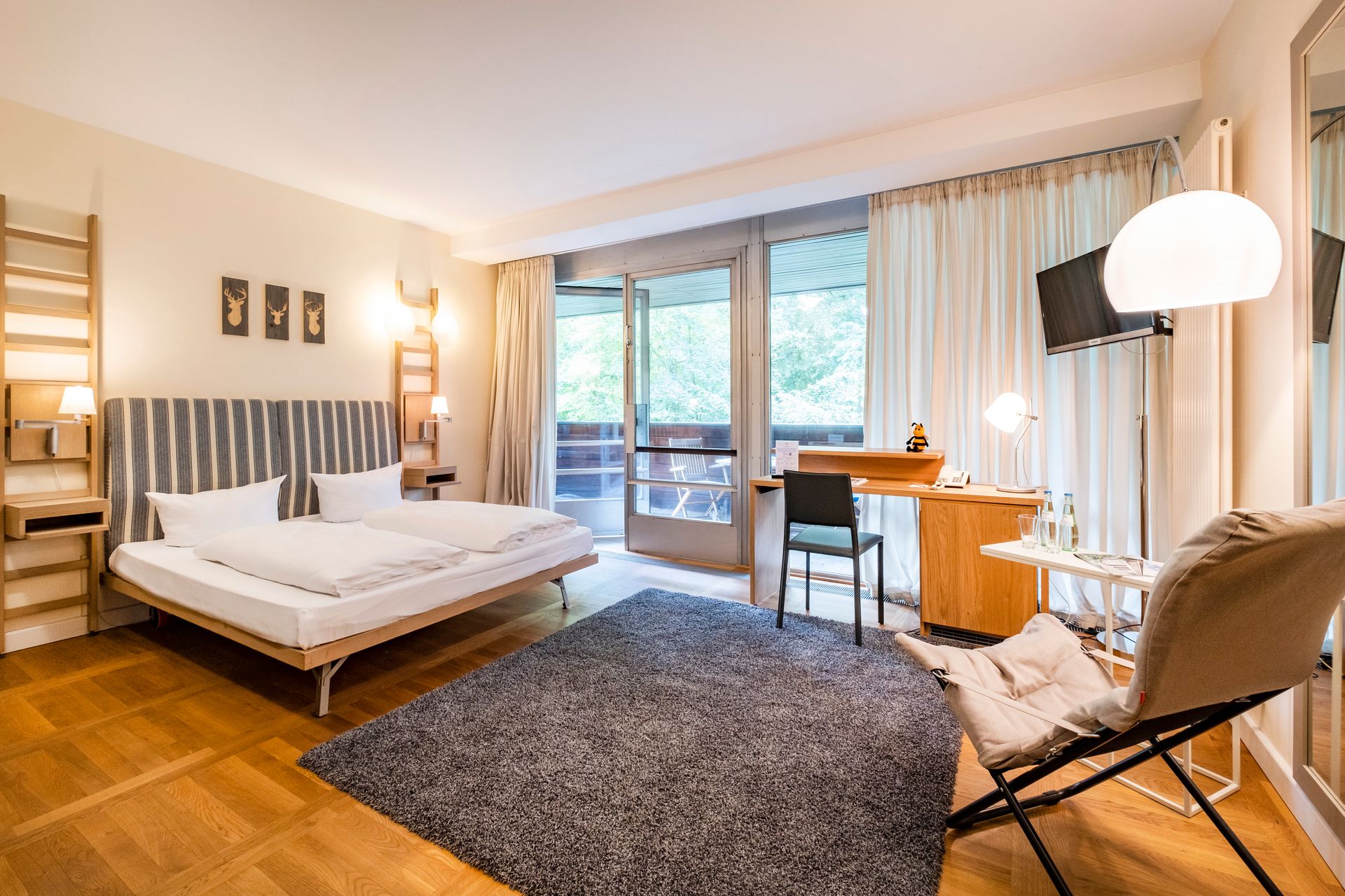 Hotelzimmer mit Bett, Schreibtisch und Balkontüren mit Blick ins Grüne.