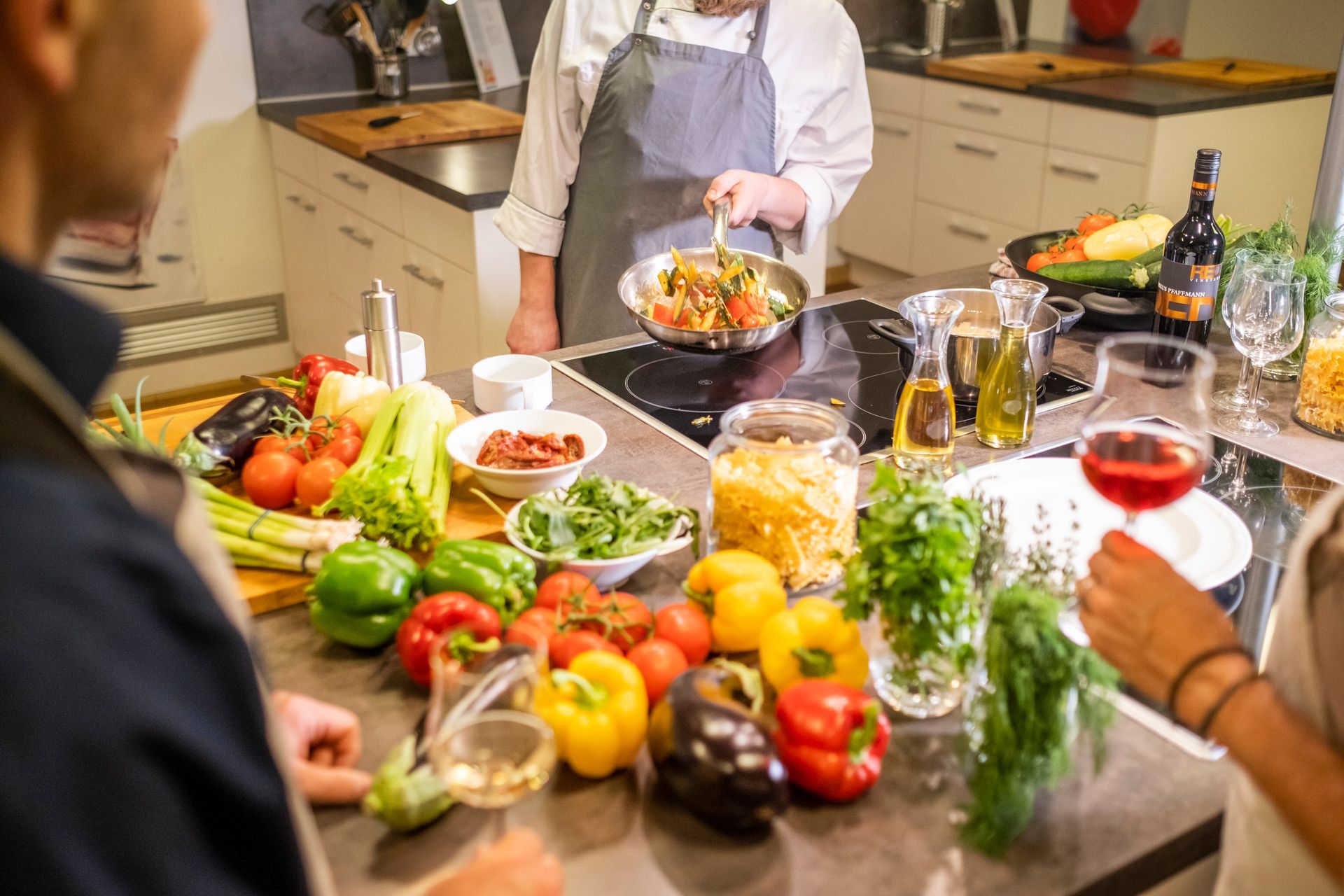 Menschen in einer Küche bereiten Essen mit frischen Produkten und Wein zu.