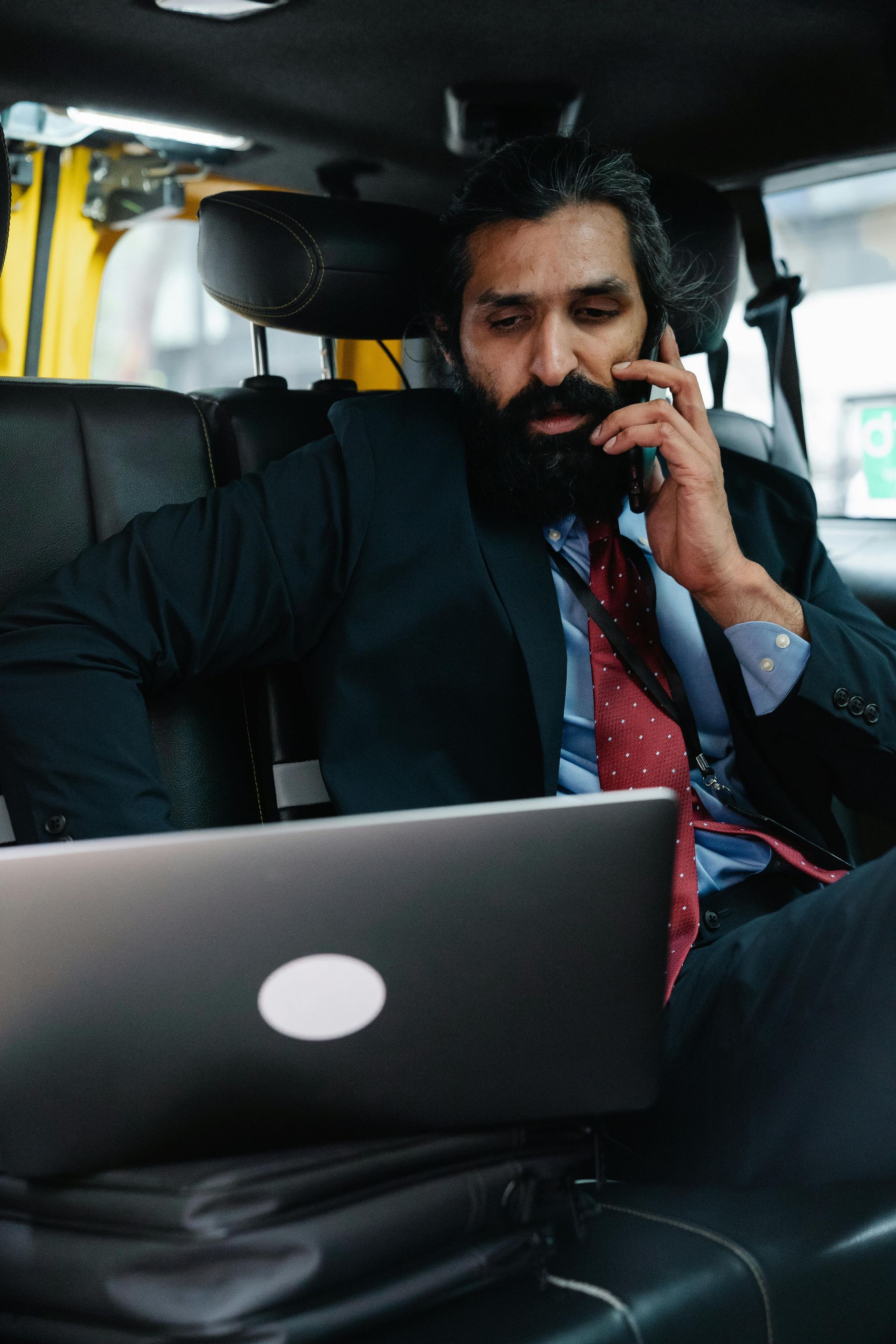 A woman is sitting in the back seat of a car talking on a cell phone.