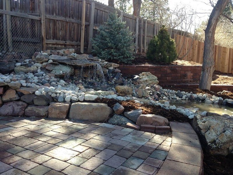 Stone patio with waterfall feature, rocks, and small trees.