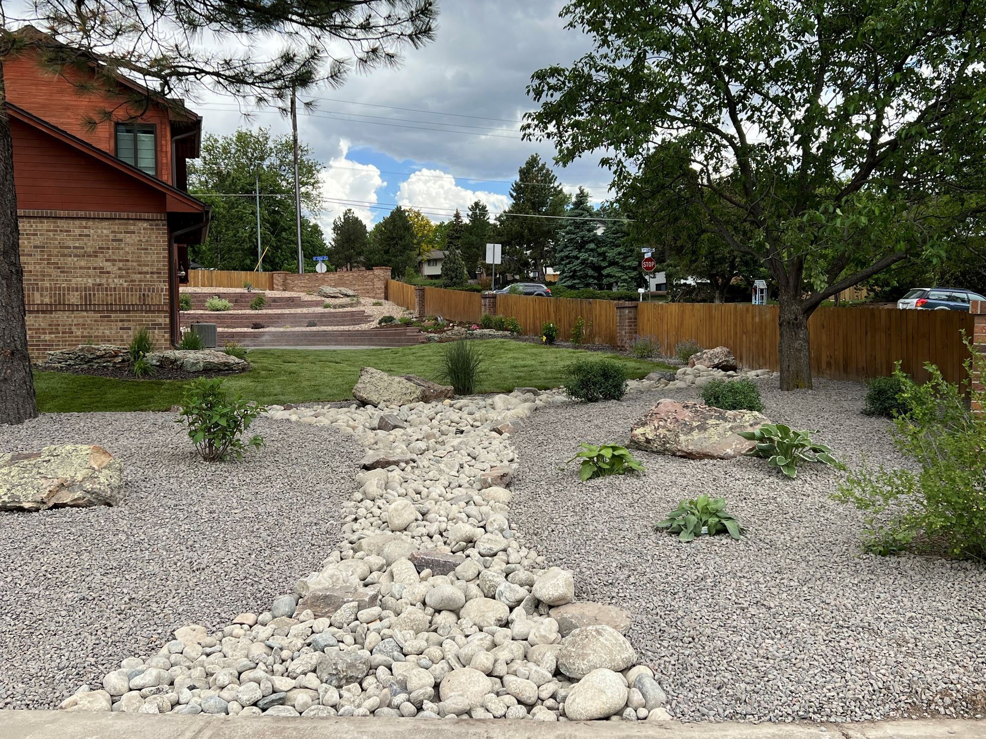 Landscaped front yard with gravel, rocks, and a dry creek bed leading to a wooden fence.