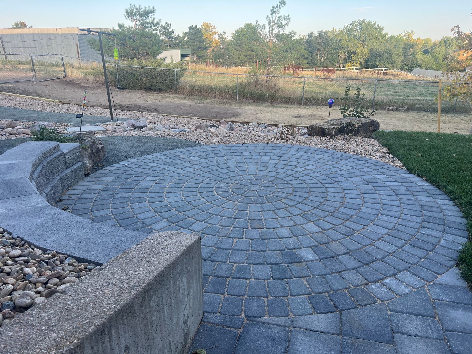 Circular paved patio with stone border, adjacent to grass and gravel landscaping.