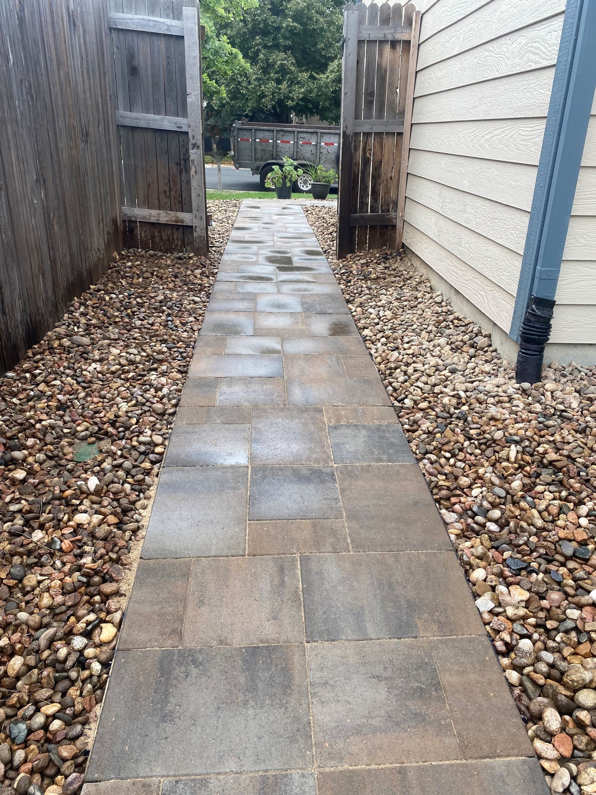 Stone pathway between fences and a building, lined with gravel.
